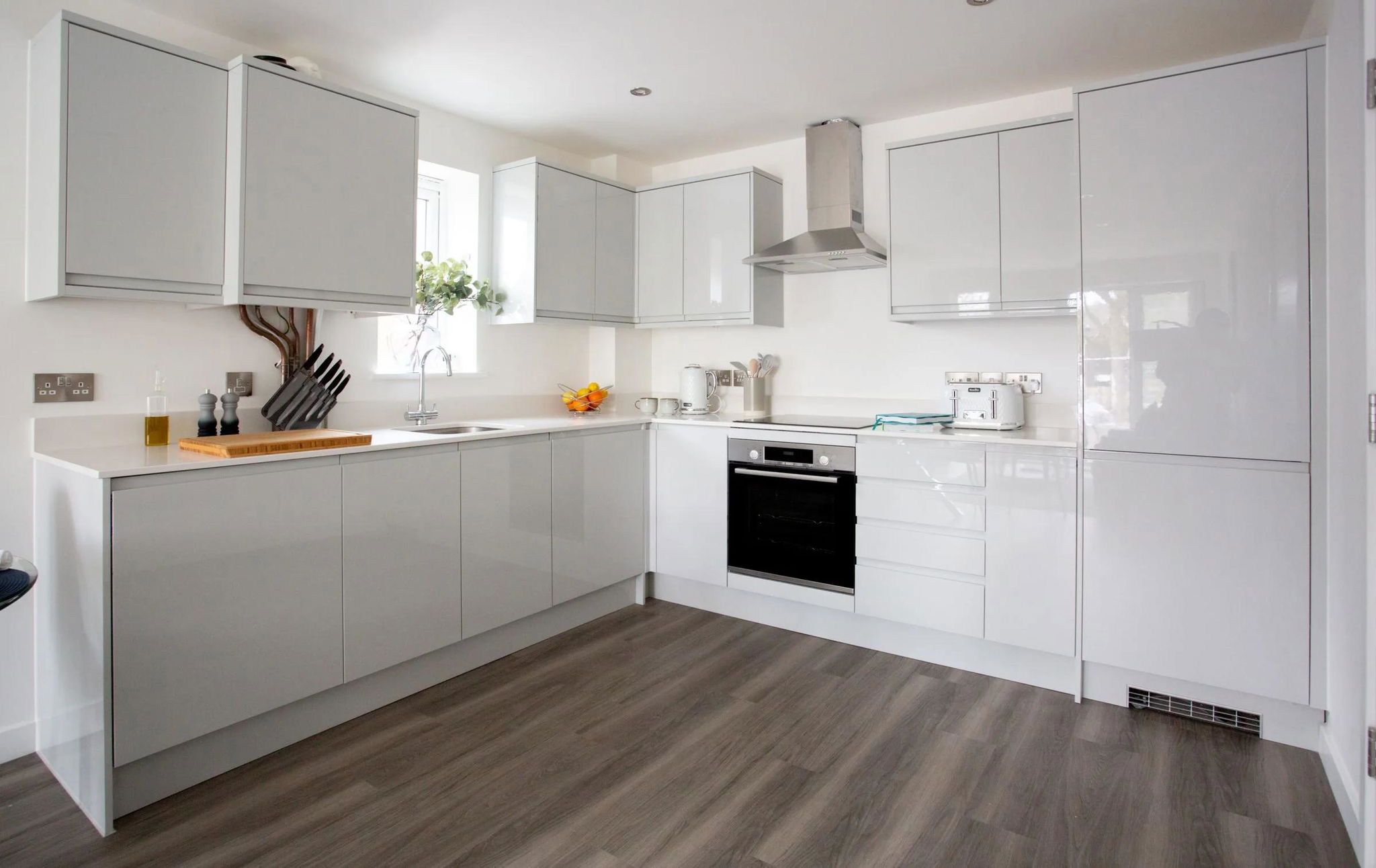 Bếp căn hộ chữ L hiện đại với lò âm tủ và tủ bếp trắng bóng — dự án căn hộ Le Phan Living